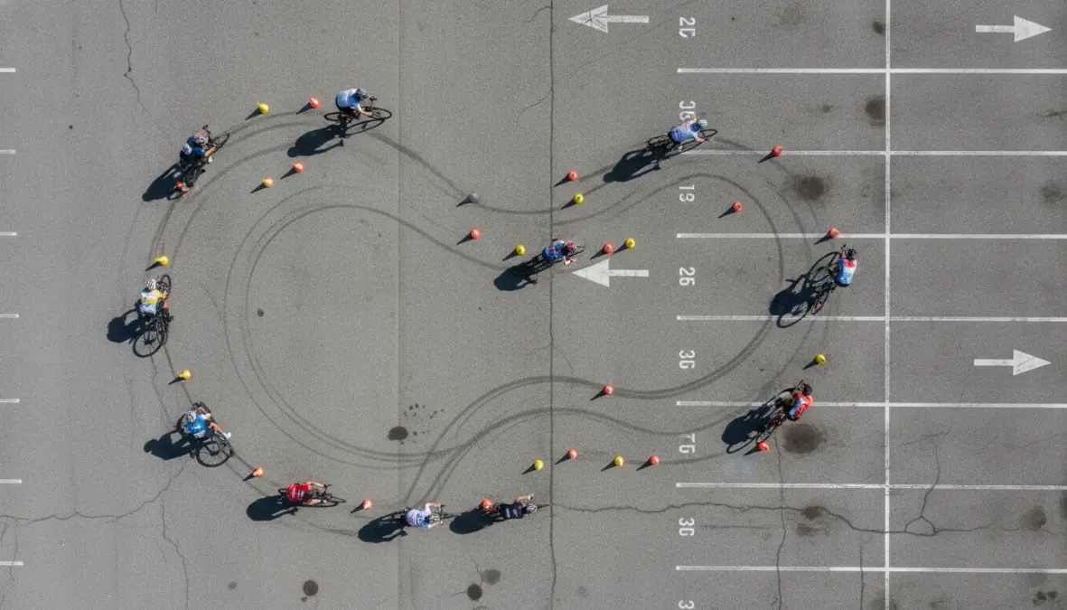 Cyclists practicing road bike cornering drills and exercises in parking lot with cones
